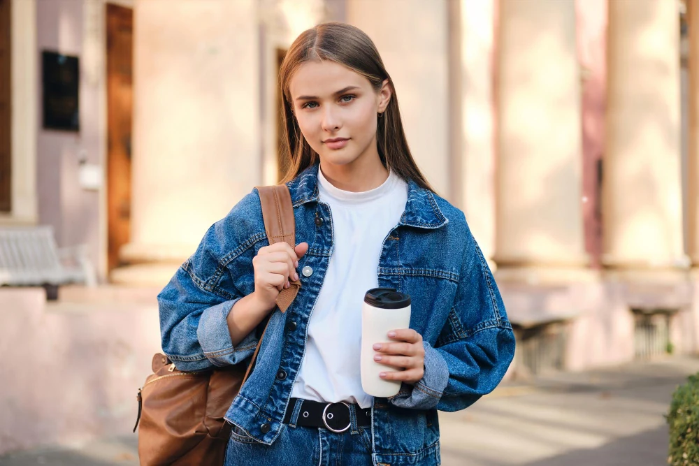 A woman carrying a backpack and coffee on a university campus
